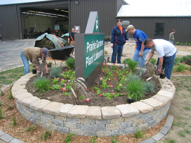 students planting around Prairie Gardens Plant Laboratory sign